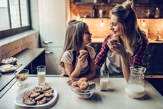 Mother and daughter eating muffins with milk in their kitchen