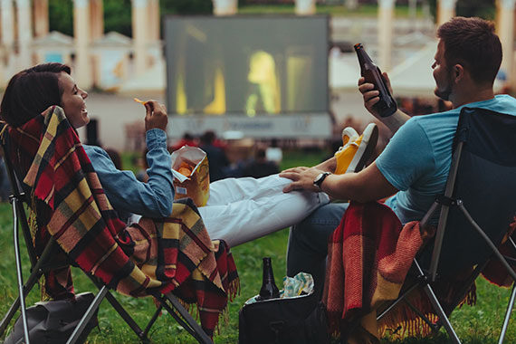 Couple sitting in chairs enjoying an outdoor movie with drinks and snacks